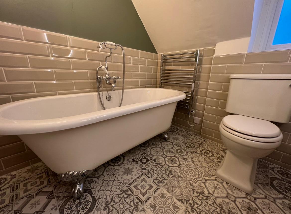 Roll-top bath with metro tiles and a patterned floor