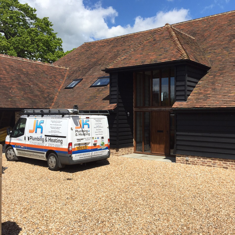 The JK Plumbing & Heating van parked outside a black weatherboarded barn